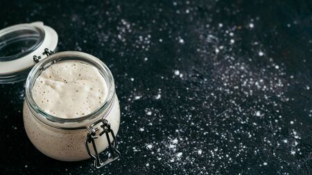 Wheat sourdough starter. Glass jar with sourdough starter on dark background, copy space.の写真素材