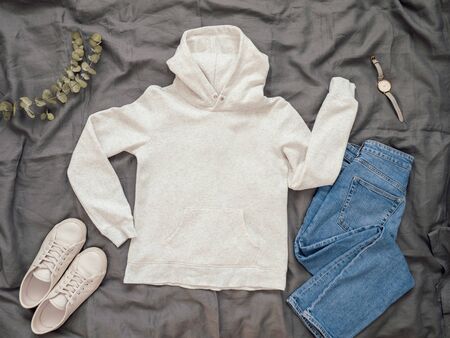 Fashionable look with white empty hoody, jeans and white sneakers. Top view of white blank hoody with long sleeves over gray bed linen. Mock up for hoody print design.の写真素材