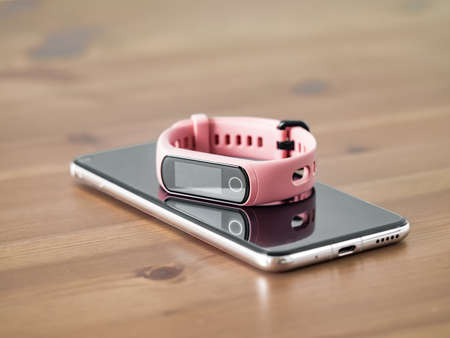 Fitness tracker on smartphone wooden tabletop. Pink female pedometer or wearable device on smartphone with infinity display, copy spaceの写真素材