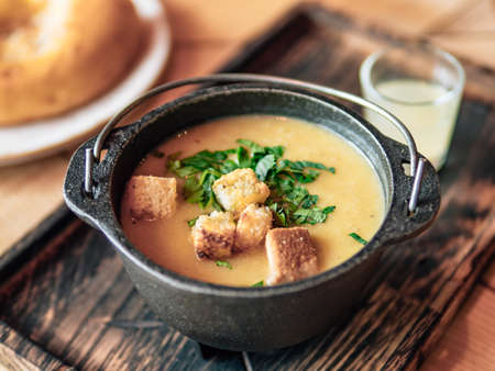 Puree soup with croutons and green parsley in old metal bowl on old wooden tray. Authentic shot of...