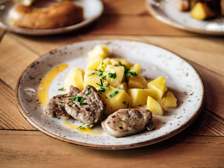 Beaf slices and boiled potatoes. Authentic shot of plate with roasted beaf or pork and potatoes on rustic wooden tabletop.の写真素材