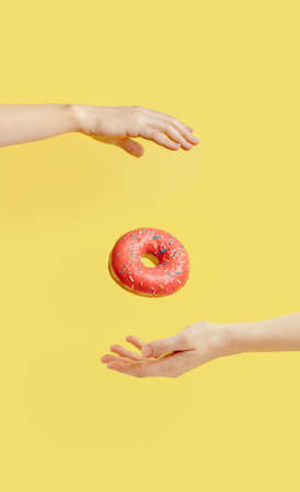 Donut falls between hands on yellow backgroundの写真素材