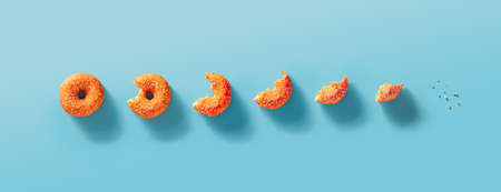 Seven stages of donut biting or eating down to crumb. Eaten donut with orange glaze and white sprinkles on blue background. Top view or flat lay. Horizontal bannerの写真素材