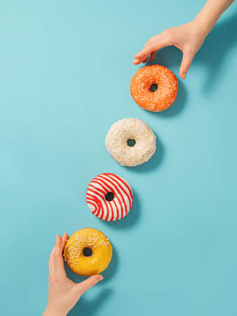 Two hands reach for donuts on blue background, top view. Creative layout with delicious glazed...