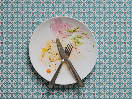 Dirty plate after healthy vegetarian paleo lunch. White plate and colorful dirty after egg yolk, beet and green pesto, over blue tablecloth. Top view or flat lay.の写真素材