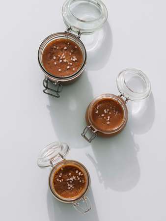Salted caramel in glass jars, top view. Brown caramel or condensed milk with sea salt crystalls, shoot in bright or hard light. Light neutral background. Verticalの写真素材