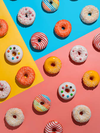 Assorted colorful glazed donuts, top view. Creative layout made from delicious glazed donuts. Vertical flat lay background with multicolored donuts or doughnuts. Blue yellow pink backdrop. Hard lightの写真素材