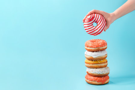 Stack of assorted donuts and one donut in female hand on blue background. Many colorful glazed doughnut with sprinkles stacked with copy spaceの写真素材