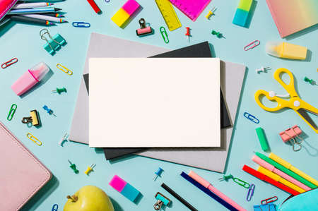 Creative student desk with white sheet of notebook paper and school supplies. Top view with copy space. Back to school flat lay on blue and pink backgroundの写真素材