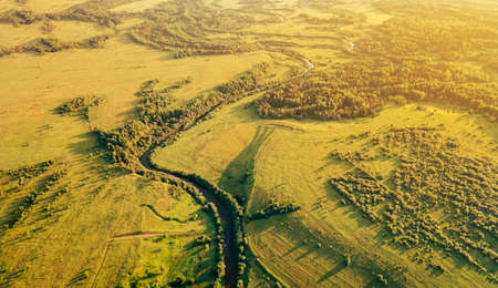 Fields and small narrow winding river aerial view. Green rural drone landscape in sunset light....