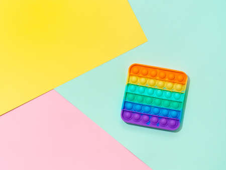 Popit or simple dimple toy on multicolor background. Popular silicone colorful antistress pop it toy for child on blue, yellow and pink paper background. Top view from above. Copy spaceの写真素材
