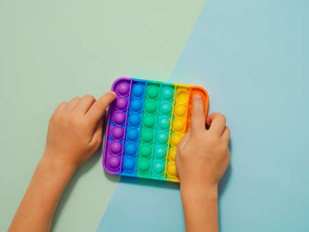 Kid hands play toy, top view over two-shadows blue background. on blue background, copy space. Popular silicone colorful anti stress toy for child. Top view from above. Simple dimpleの写真素材
