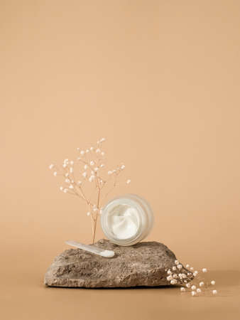 Cosmetic cream or moustirizer on stone over pastel beige background. Open round glass jar with aesthetic swirls face cream and spatula. Copy space. Vertical. Mockupの写真素材