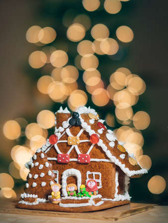 Christmas gingerbread house decoration on background of defocused golden lights of Christmas tree. Vertical. Copy space. Gingerbread house cake with bokeh as concept Christmas, Happy new year holidaysの写真素材