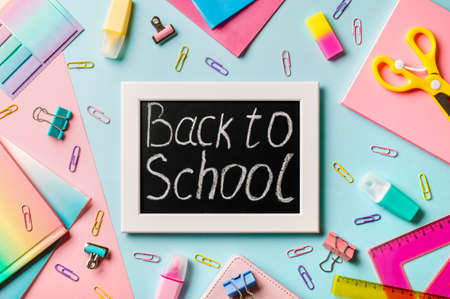 Blackboard with letters Back to school made with chalk. School supplies, pencils, scissors and colored books on blue and pink background. Top view or flat lay. Back to school conceptの写真素材