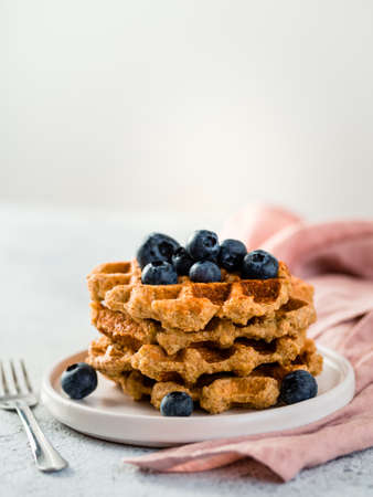 Easy healthy gluten free oat waffles with copy space. Stack of appetizing homemade waffles with oat flour decorated blueberries, on plate over light gray cement background. Verticalの写真素材