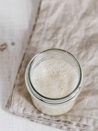 Wheat sourdough starter. Top view of glass jar with sourdough starter on white wooden background. Copy space for text or design. Vertical.の写真素材