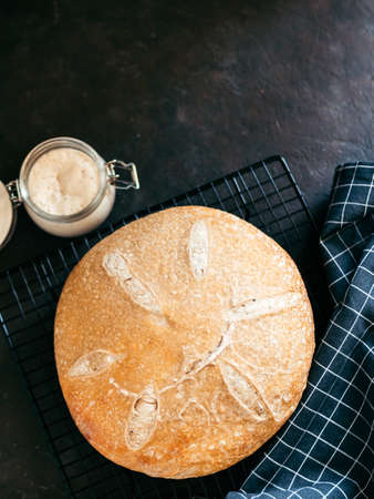Wheat round sourdough bread and sourdoug starter in glass jar. Top view of delicious homemade sourdough bread on black background with copy space. Home made sourdough bread making concept. Vertical.の写真素材