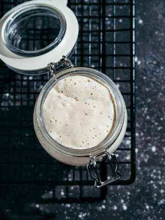 Wheat sourdough starter. Glass jar with sourdough starter on dark background, copy space. Vertical.の写真素材