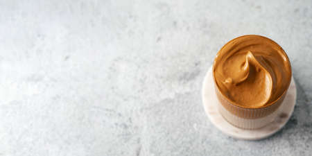 Trendy korean drink - dalgona coffee. Glass jar with cold or hot beverage - whipped instant coffee with milk on gray cement background with copy space. Top view or flat lay. Bannerの写真素材