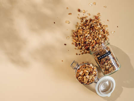 Homemade granola sprinkled of glass jar over pastel beige background. Top view or flat lay. Aesthetic oat granola, beautiful shadows, champagne yellow background. Healthy breakfast conceptの写真素材