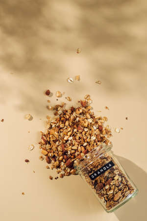 Homemade granola sprinkled of glass jar over pastel beige background. Vertical. Top view or flat lay. Aesthetic oat granola, beautiful shadows, champagne yellow background. Healthy breakfast conceptの写真素材