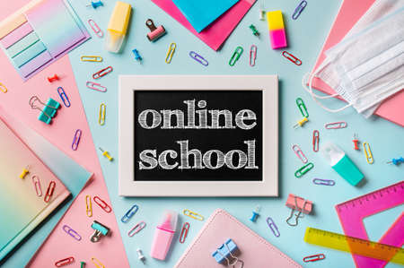 Black chalkboard with letters online school. School supplies, pencils, scissors and colored books on blue and pink background. Top view or flat lay. E-learning conceptの写真素材