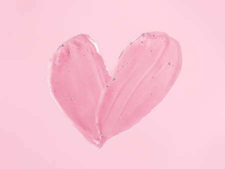 Liquid gel cosmetic smudge texture in heart shape on pink background. Aesthetic beautiful textured smear transparent skin gel or face mask like heart. Top view or flat layの写真素材