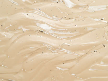 Liquid gel cosmetic texture on beige nude background. Aesthetic beautiful textured smears transparent skin gel with waves. Top view or flat lay. Champagne color gel backgroundの写真素材