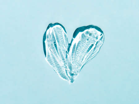 Liquid gel cosmetic smudge texture in heart shape on blue background. Aesthetic beautiful textured smear transparent skin gel or face mask like heart. Top view or flat layの写真素材
