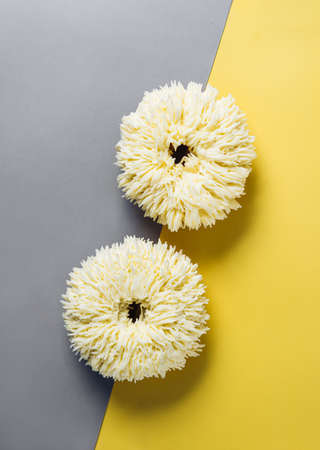 Shag donuts on two color gray and yellow background. Unusual trendy donuts with white vanilla buttercream. Copy space. Top view or flat lay. Verticalの写真素材