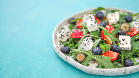 Salad with arugula, feta cheese and berries - strawberry, blueberry, in craft plate. Summer salad...