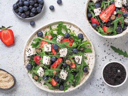 Salad with arugula, feta cheese and berries - strawberry, blueberry, in craft plate on gray cement bacground. Summer salad idea and recipe for healthy vegetarian lunch, dinner. Top view. Copy space.の写真素材