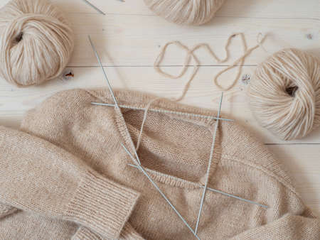 Knitting project in progress. Beige wool sweater in knitting process neckopening and making neck. Top view image to illustrate of how to knit neck of sweater with knitting needles. Female hobby knittingの写真素材