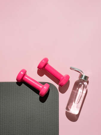 Stylish gray, water bottle and pink fitness training and gym flat lay. Top view of gray sport mat and pink dumbbells on pink background. Set for pilates, fitness with copy space. Veticalの写真素材