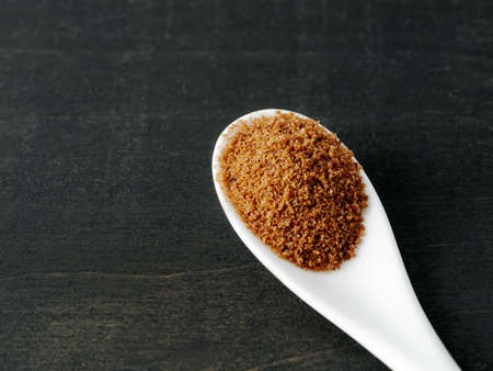 Spoon of coconut brown sugar on dark wooden background. Top view of full white ceramic spoon with raw organic coconut sugar from crystallized sap of cut flower buds coconut palm. Copy space. Closeupの写真素材