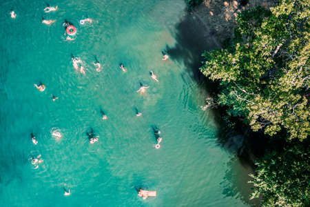 Aerial drone top down view of unrecognizable people swimming in lake. Beautiful blue water with many people rest on beach, swimming and jumping in pond or river. Summer time at lake, drone shotの写真素材