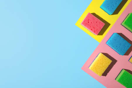 House cleaning sponges on blue, pink, yellow background, copy space. Flat lay or top view. Cleaning service or housekeeping concept with space. Hard shadows in sunlightの写真素材