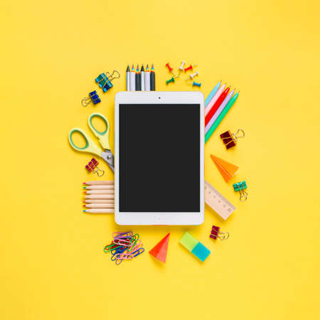Online study, distantly learning class. Online education, back to school, freelancer work concept. Tablet pc and school supplies, stationery accessories on colored yellow background. Flatlay, top viewの写真素材