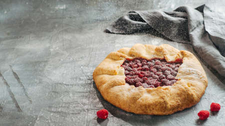 Raspberry galette with copy space. Powdered sugar poured onto delicious rustic homemade tart with frozen or fresh raspberries on gray backgroundの写真素材