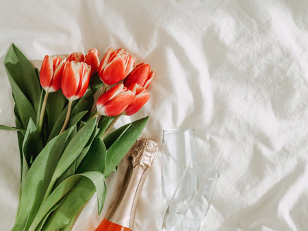 Bunch of red tulips, rose wine and champagne glasses on white bed sheets. Valentines day, date, march 8 concept. Spring flowers and bottle aesthetics. Top view or flat lay. Copy spaceの写真素材