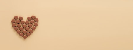 Heart made from chocolate candies. Chocolate hearth on pastel beige background. Long horizontal banner for Valentines Day, champagne yellow background. Copy space. Top view or flat layの写真素材