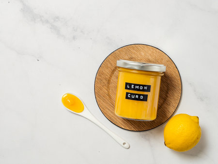 Delicious homemade lemon curd. Glass jar with lemon curd and full spoon on white marble background. Black sticky label with text Lemon Curd on jar. Top view or flat lay. Copy spaceの写真素材