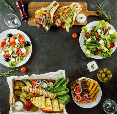 Greek food assorted with copy space in center, on dark background. Gyros, greek salad, souvlaki, grilled vegetables - selected of greek cuisine assortmentの写真素材