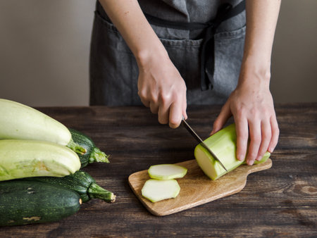 Zucchini harvest. Woman slices zucchini on wooden table. Farm organic zucchini harvestingの写真素材