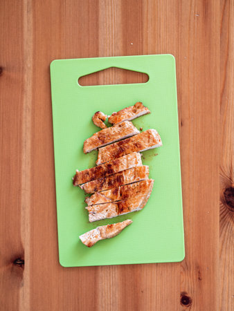 Grilled turkey meat steak sliced on cutting board over wooden tabletop. Perfect ready-to-eat turkey fillet on green cutting board top view or flat lay. Striped cooked fillet of turkey meat. Verticalの写真素材