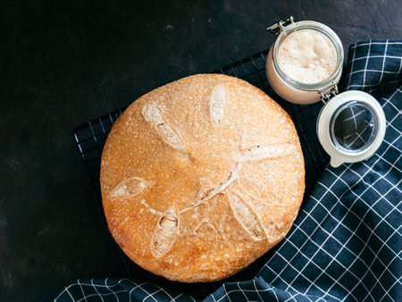 Wheat round sourdough bread and sourdoug starter in glass jar. Top view of delicious homemade sourdough bread on black background with copy space. Home made sourdough bread making concept.の写真素材