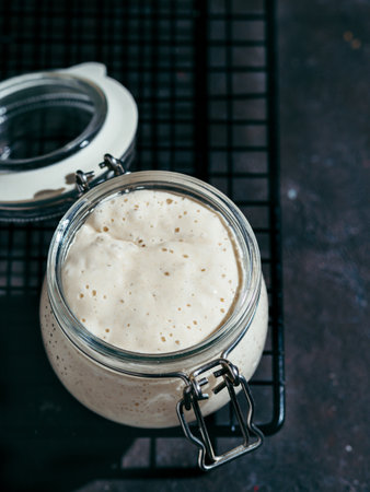 Wheat sourdough starter. Glass jar with sourdough starter on dark background, copy space. Vertical.の写真素材