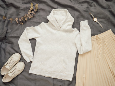 Fashionable female look with white empty hoody, cream pleated skirt and white sneakers. Top view of white blank hoody with long sleeves over gray bed linen. Mock up for hoody print design.の写真素材