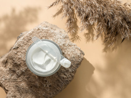 Cosmetic cream or moustirizer on stone, pampas grass on pastel beige background. Beautiful shadows. Open round glass jar with aesthetic swirls face cream and spatula. Flatlay. Copy spaceの写真素材